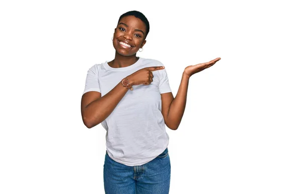 手で提示し 指で指している間若いアフリカ系アメリカ人女性は カジュアルな白いTシャツを着てカメラに驚いて笑顔 — ストック写真