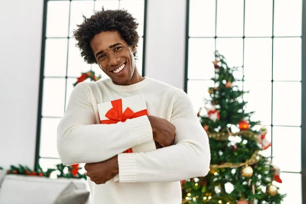 Joven Afroamericano Hombre Sosteniendo Regalo Pie Junto Árbol Navidad Casa — Foto de Stock