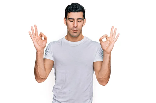 英俊而惊慌的男人穿着宽松的白色T恤 闭着眼睛微笑着 用手指做冥想动作 瑜伽概念 — 图库照片