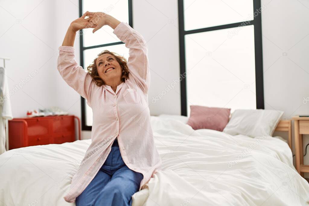 Middle age caucasian woman waking up stretching arms at bedroom.