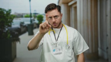 Doktor, şehir sokağında ciddi bir ifadeyle işaret ediyor. Steteskoplu genç adam dışarıda bekliyor..