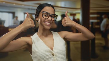 Mutlu kadın otelin lobisinde olumlu bir tavır sergiliyor. Büyük bardaklar ve gülümseyen yüz ifadesi kapalı mekan atmosferini ve konukseverliği arttırıyor.