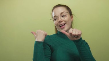 Gözlük takan ve yeşil kazak giyen kadın yeşil stüdyoda kendini geri çekiyor..