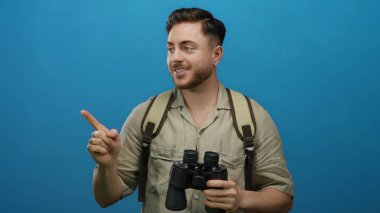 Elinde dürbün tutan sakallı ve sırt çantalı genç bir adam mavi bir arka plana bakıp gülümsüyor, keşif ve seyahat etmeyi öneriyor..