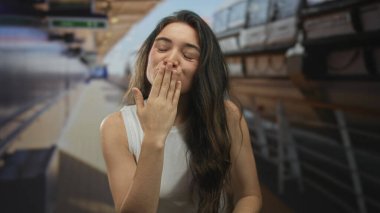 Beyaz kolsuz tişörtlü bir kadın, güneşli tekne güvertesinde dudaklarından öpücükler saçıyor, uzun saçları rüzgarda uçuşuyor, sevgi dolu..