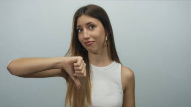 Gri stüdyoda parmak, uzun saç ve tarafsız ifadeyle baş parmak gösteren Latin asıllı genç bir kadın..