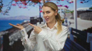 Deniz kenarındaki bir gezinti alanında, arka planda canlı çiçekler ve okyanus manzarası olan neşeli bir anda kadın jestleri yapıyor..