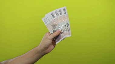 İzlanda krona banknotları tutan adam, canlı sarı bir arka plana karşı, beyaz bir erkek eli ile izole bir fon üzerinde belirgin bir para sergiliyor.