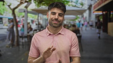 Pembe polo tişörtlü bir adam güneşli bir öğleden sonra kafenin dışındaki terasta el çırpıyor..