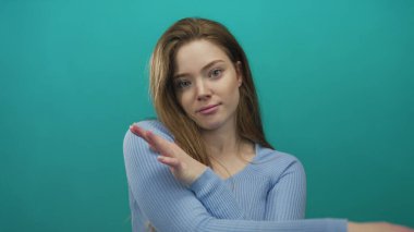 Stüdyoda iki eli kapalı, yumuşak gülüşlü, kollarını kendine doğru uzatan genç bir kadın..