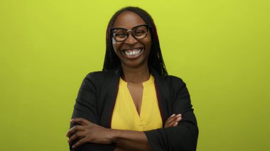 Güvenle gülümseyen bir kadın, kolları bağlı, parlak sarı bir arkaplanda neşeli ve cana yakın tavrını sergiliyor..