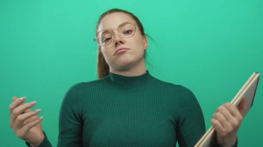 Genç kadın yeşil stüdyo duvarına karşı not defteri tutuyor. Aşağıya doğru bakan bakışlar ve büzüşmüş dudaklarla karalıyor. Can sıkıntısı..