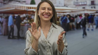 Tedarikçi tezgahının yanındaki çizgili tente altında el çırpan kadın, mutluluğu kutluyor..