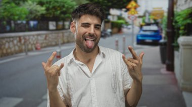 Meşgul caddede iki elle boynuz hareketi yaparken insan sırıtıyor ve dil gösteriyor..