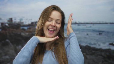 Güneşli sahilde gülümseyen ve çerçeveli yüzü olan beyaz bir kadın; neşe verici yaratıcılık güveni.
