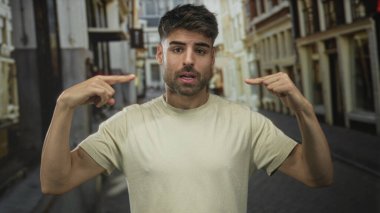 İspanyol asıllı genç adam güneşli bir şehir caddesinde kendini işaret ederek bina cephelerinin etrafını sardı..