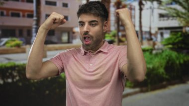 Öğleden sonra güneşli bir şehir sokağında yumruklarını sıkan ve enerjik bir şekilde gülümseyen İspanyol genç adam..