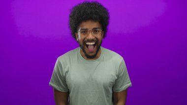 Gözlüklü Afro-Amerikalı adam mutluluk ve enerji gösteren canlı bir mor arka plana gülümsüyor..