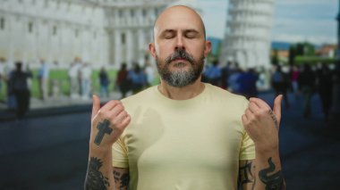 Dışarıdaki pisa kulesinin önünde sakince meditasyon yapan adam sakin bir sokak ortamında dövmelerini ve sakallarını sergiliyor..