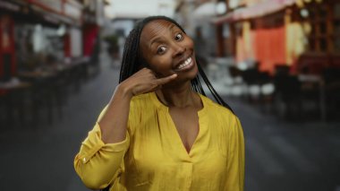 Sarı tişörtlü bir kadın, şehir sokaklarında gülümserken telefonla konuşuyor, mutluluk ve bağlantıyı vurguluyor..