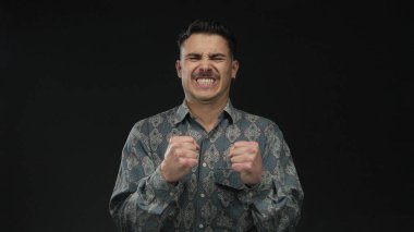 İzole edilmiş siyah arkaplan duvarına karşı duygularını ifade eden genç bir adam değişik ruh hallerinde desenli bir gömlek giyiyor dinamik ifade ve stil aktarıyor.