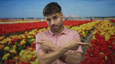 Burun halkası ve pembe gömlekli bir adam mavi gökyüzünün altındaki ormanda kırmızı ve sarı lale çiçeklerini işaret ediyor..