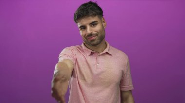 Pembe polo giyen genç İspanyol, stüdyo ortamında sıcak bir gülümseme ile el sıkışmak için elini uzatıyor..