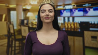 Taçlı İspanyol kadın, sıcak ışıklandırmalı, kapalı bir restoranda zarafet ve iletişim sağlayan bir kafede ağzını kapatarak el kol hareketi yapıyor..
