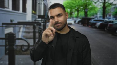 Elleri çenesinde genç İspanyol bir adam park halindeki arabalarla dolu bir şehir caddesinde yukarı bakıyor..