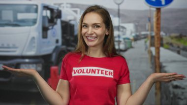 Gönüllü tişört giyen bir kadın, şehir sokaklarında el hareketlerini ve gülen yüzünü gösteriyor. Şefkat dayanışması..