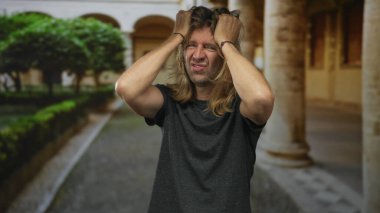 Erkek, binadaki uzun sarı saçları hem gerilmiş kolları hem de büzüşmüş dudakları, yukarı bakan gözleri, stresi kavrar..