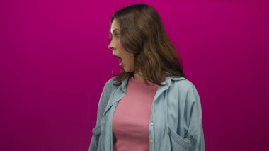 Pembe gömlekli ve mavi ceketli bir kadın, canlı morumsu arka planda izole edilmiş bir şekilde stüdyo ortamında dışa dönük tepkiler verirken şaşırdı..