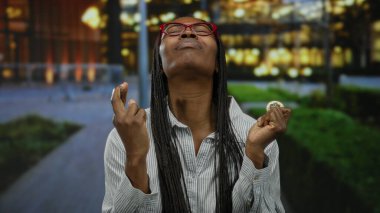 Uzun saçlı ve gözlüklü bir kadın şehir ortamında Cardano sikkesini elinde tutuyor. Bulanık bir şehir arka planına sahip umut ve güveni ifade ediyor..