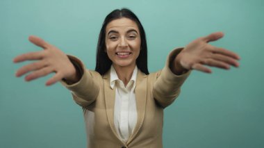 Elleri yeşil duvara uzanmış, bej ceketli ve beyaz gömlekli İspanyol kadın el kol hareketi yapıyor..