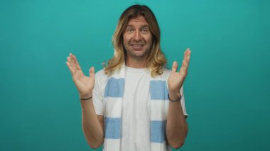 Çizgili futbol eşarbı takan sarışın adam, stüdyoda tezahürat jestinde elini kaldırıyor; takım desteği coşkusu.