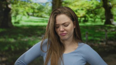 Güneşli bir parkta, yeşil ağaçların ve çimenlerin ortasında, yüzü buruşmuş ellerle kaşlarını çatan kadın iğreniyor..