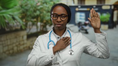 Şehir sokaklarında steteskoplu kadın doktor bağlılık ve güvenini gösteren yeminli bir jestle elini kaldırdı..