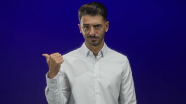 Mavi stüdyoda, parlak ışık altında solu gösteren bir adam. Kendinden şüphe eden belirsizlik..