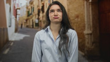 Dalgalı saçlı, mavi gömlekli kadın sabah güneşinin altında eski kasaba sokağında dudakları dudaklı; can sıkıntısı..