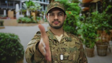 Kamuflaj üniformalı adam, saksı bitkileriyle dolu kalabalık şehir caddesinde el sıkışmak için elini uzattı; dayanışma.