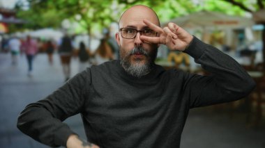 Şehir sokaklarında barış jesti yapan bir adam canlı yeşil arka plan ve bulanık kafeterya atmosferi ile.