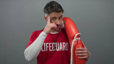 Kırmızı tişörtlü genç İspanyol cankurtaran gri duvara karşı can simidiyle poz veriyor, baş istihbaratı yapıyor ve tetikte bekliyor..