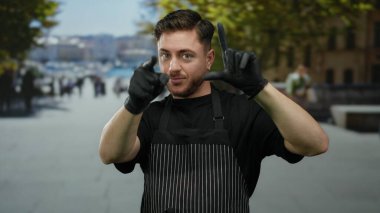 Önlüklü, sakallı genç adam sokaklarda eldivenler giyerek ezik jestler yapıyor..