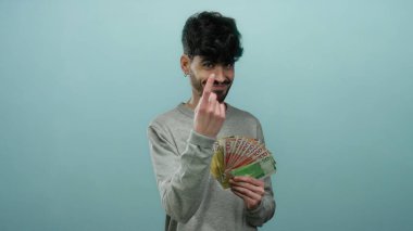 İzole edilmiş mavi arka plana karşı Norveçli kronu tutan adam, servetini güvenle gösteriyor.