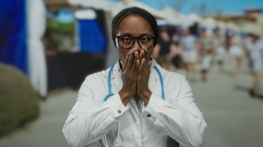 Beyaz önlüklü ve gözlüklü kadın. Şehir sokağında dikiliyor. Arka planda bulanık kalabalık ve binalar var..