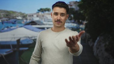 Şehir merkezindeki bulanık geçmişi olan Latin kökenli genç adam açık mavi gökyüzü altında davetkar bir jest sergiliyor.