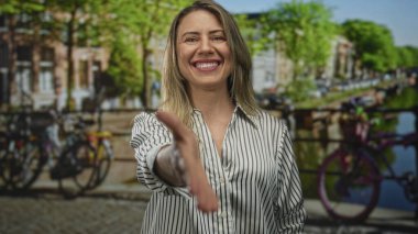 Kadın, çizgili gömlekli ve neşeli gülümsemeli yeşil stüdyo arkaplanına el sıkışmak için elini uzatıyor; güven bağlantısı.