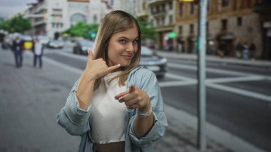 Sarışın kadın çağrı işareti yapıyor ve kalabalık şehir caddesinde kamerayı işaret ediyor; eğlenceli bir davet.