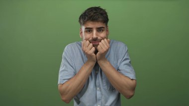 Stüdyoda soluk mavi gömlekli ve kollarını görünür şekilde sıkan bir adam yeşil ışık altında; endişe şüphesi.