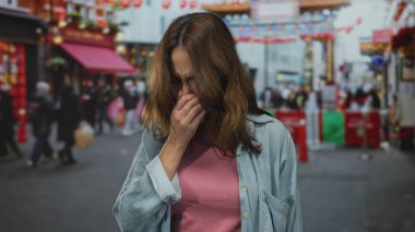 Meşgul şehir caddesinde pembe gömlekli bir kadın endişeli bir ifadeyle burnunu kapatırken kalabalık parlak kentsel arka planla süslü kemer yolunun altından geçiyor.